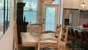 Un comedor con mesa y sillas de madera, una lámpara colgante y una cocina al fondo.