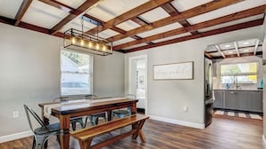 A dining area with a wooden table and benches, a kitchen with gray cabinets, and a ceiling with exposed beams.