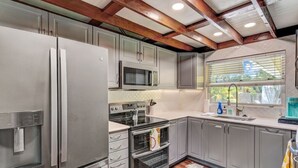 A modern kitchen with stainless steel appliances, grey cabinets, and a wooden ceiling.