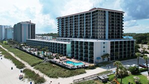 A multi-story hotel with a rooftop pool, surrounded by a beach and greenery.