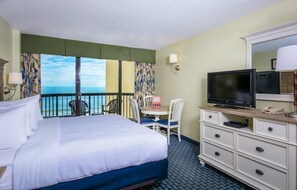 Habitación de hotel con cama, televisión, escritorio y una silla, y vista al océano.
