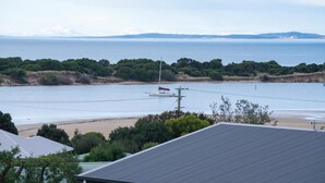 Vista costera con playa, un velero y una casa de techo inclinado.