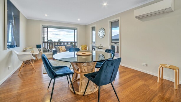 Una sala de estar moderna con una mesa de comedor de vidrio rodeada de sillas, un ventanal con vistas y un balcón.