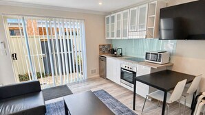 Een moderne keuken met witte kasten, een magnetron en een eethoek met een tafel en stoelen.
