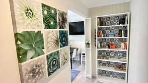 Een gang met een boekenkast, een televisie en een muur met verschillende plantenafdrukken.