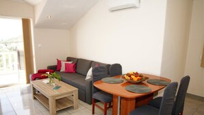 A modern living room with a sofa, a dining table with chairs, a coffee table, and a fruit bowl. - Apartments Mi&Ni - One Bedroom Apartment with Balcony and Sea View (Cavtat)