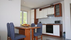 A modern kitchen with white cabinets, a microwave, and a dining area with a table and chairs. - Apartments Mi&Ni - One Bedroom Apartment with Balcony and Sea View (Cavtat)