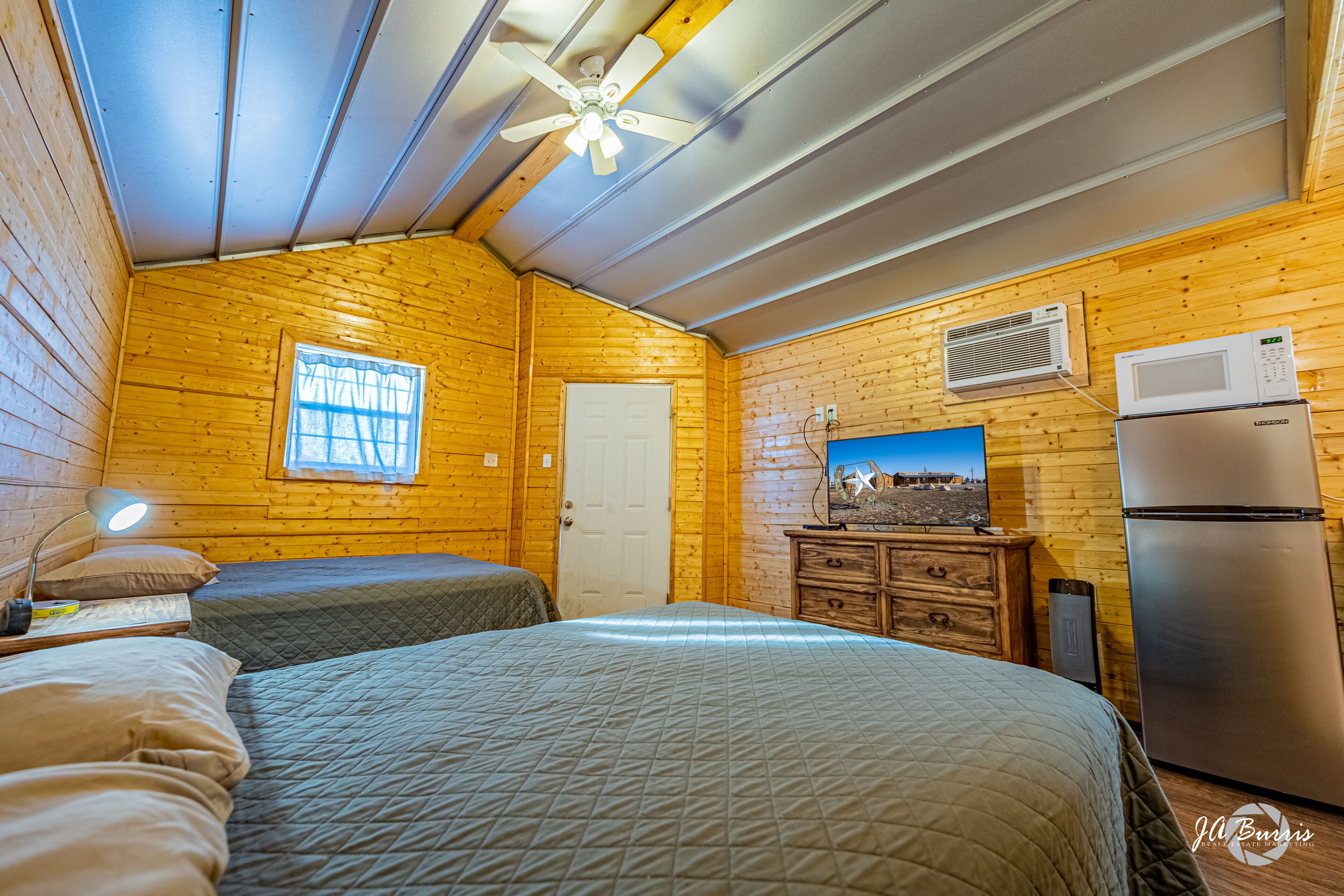 Um quarto acolhedor no estilo de cabana, com duas camas, um ventilador de teto, um micro-ondas e uma geladeira.