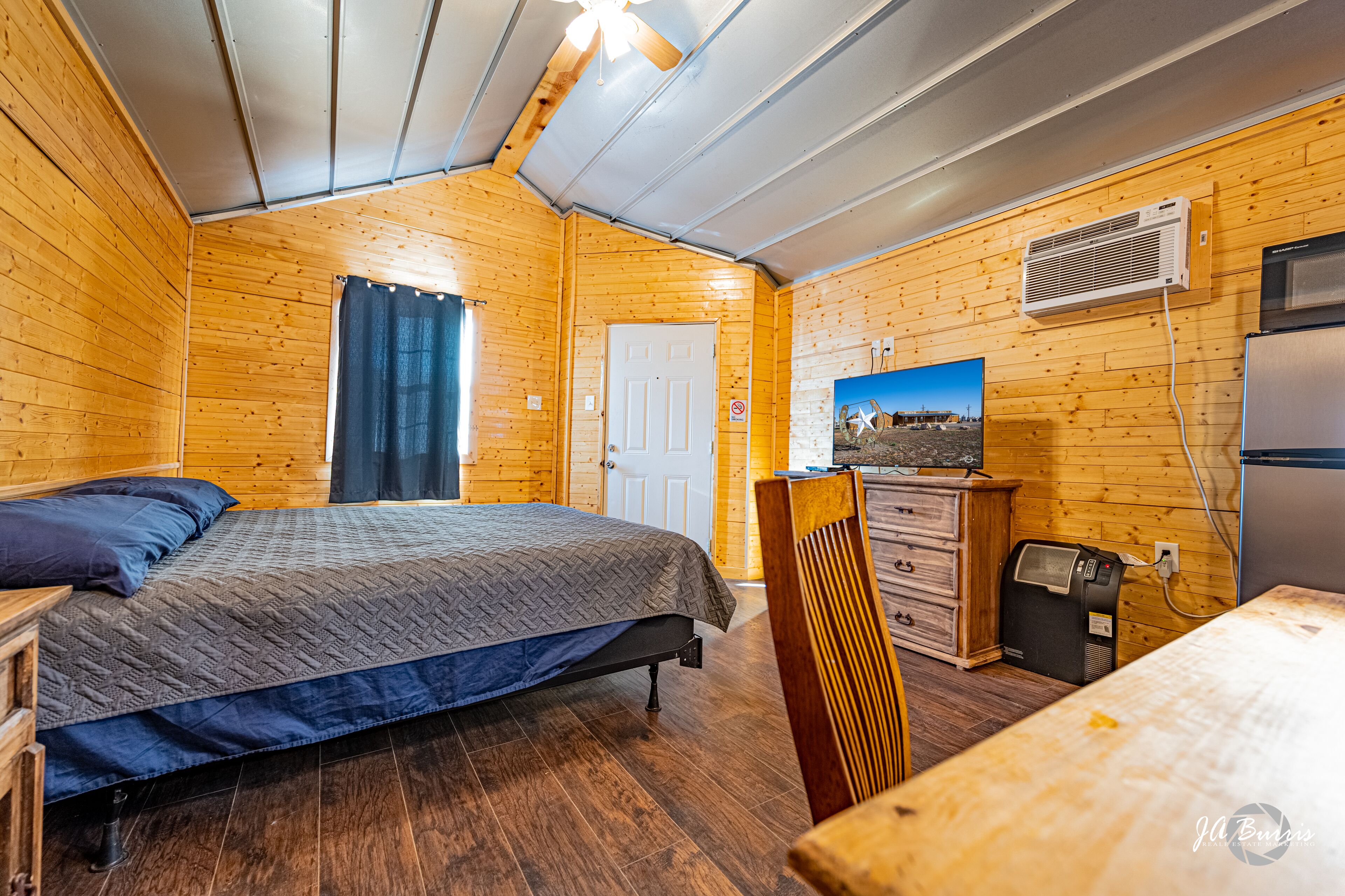 Quarto de cabana de madeira com cama, cómoda e cozinha compacta.