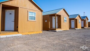 Une rangée de cabanes en bois, chacune dotée d’une porte numérotée et d’une petite fenêtre située au-dessus de la porte.