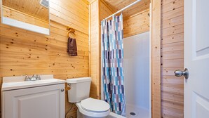 Une salle de bain avec des murs en bois, des toilettes, un lavabo et une douche avec un rideau à carreaux.