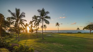 Un parcours de golf bordé de palmiers, offrant une vue sur l’océan au coucher du soleil.