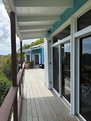 A covered wooden deck with sliding glass doors leading to a covered patio area.