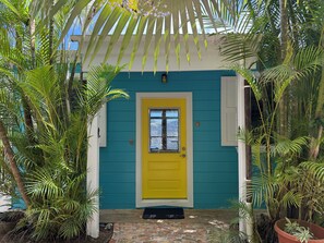 A house with a yellow door, surrounded by lush greenery and a blue exterior.