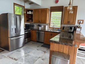 A modern kitchen with stainless steel appliances, wooden cabinets, a granite countertop, and a window with a view of greenery.