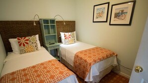 Una habitación con dos camas, cada una con una colcha y cojines estampados, una mesita de noche con lámpara y un mueble auxiliar pequeño.