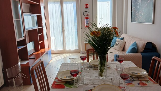 Ein Essbereich mit einem Tisch für vier Personen, einer Blumenvase und einer Couch im Hintergrund.