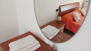 Ein Hotelzimmer mit Bett, Nachttisch, Spiegel, Holzkommode und einer Glasvase mit Blumen.