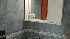 Ein Badezimmer mit einem weißen Waschbecken, einem Spiegel darüber und einer gefliesten Wand.