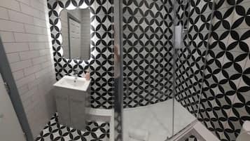 A bathroom with a black and white geometric tile pattern, a white sink, and a glass shower enclosure.