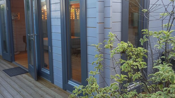 A building with a wooden deck, a black exterior light fixture, and a door leading to a room with a visible interior. - Sandy Toes Accommodation (Par)