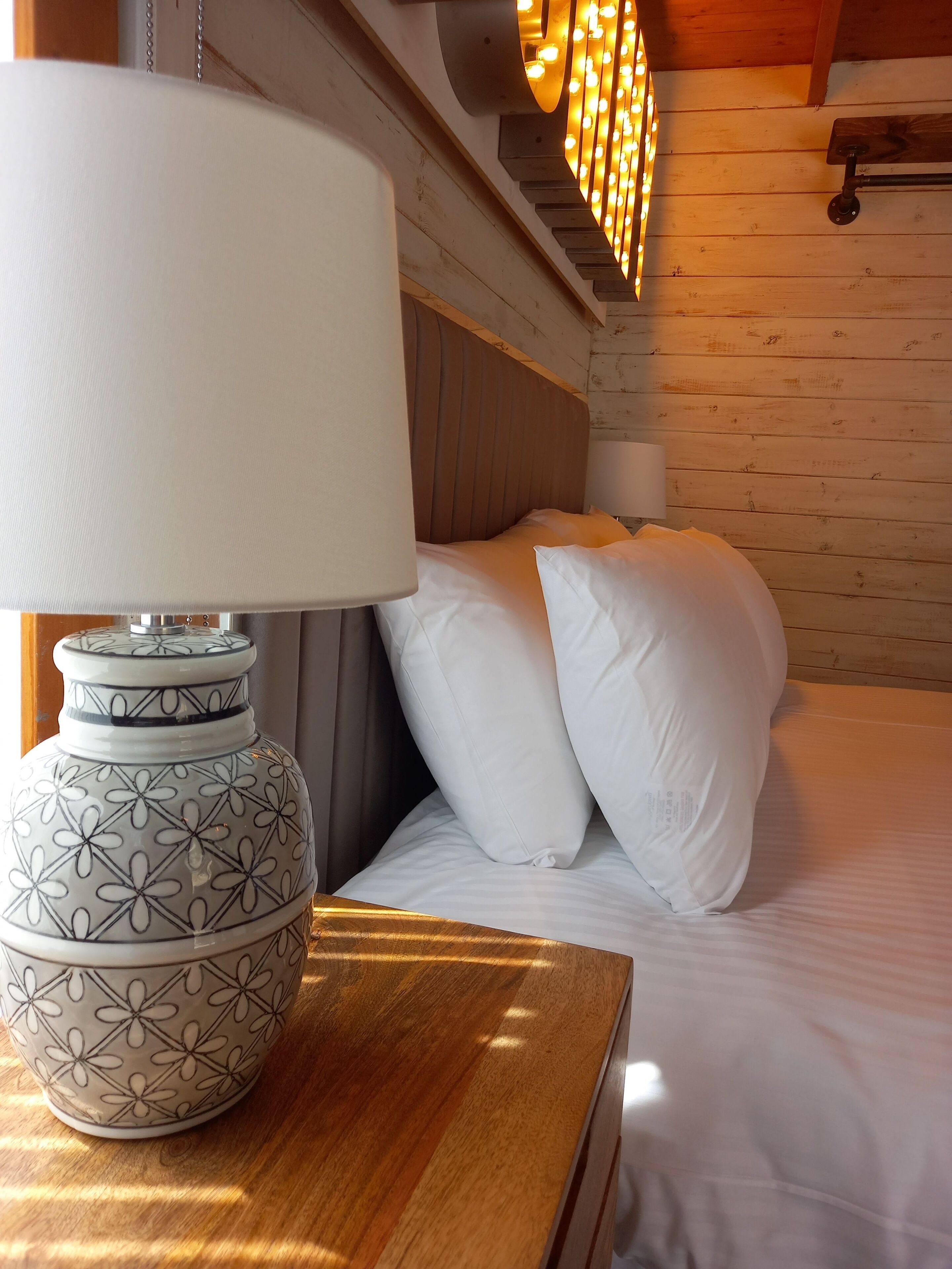 Ein Bett mit weißer Bettwäsche und Kissen, ein Holzkopfbrett und eine dekorative Lampe auf einem Nachttisch.