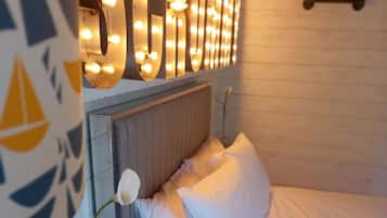 A neatly made bed with white linens, a bedside table with a vase of flowers, and a wall-mounted light fixture spelling out "SCRUBBED".