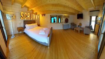 A cozy wooden cabin bedroom with a large bed, a vanity, a chair, and a TV.