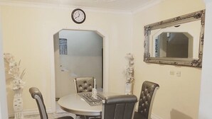 Un coin repas avec une table ronde, quatre chaises, une horloge et un miroir au mur.