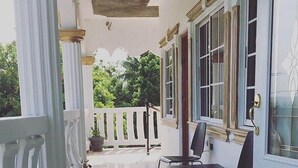 Un espace extérieur abrité, doté d’un sol carrelé, d’une rambarde blanche et d’une table avec des chaises.