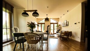 Un amplio salón con una mesa de comedor, sillas y un sofá. Hay un ventanal con persianas, una chimenea y una lámpara en el techo.