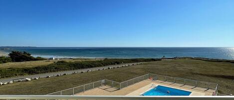 Un balcon avec vue sur une piscine et l’océan.