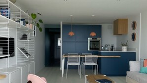 Un soggiorno moderno con una poltrona a dondolo rosa, un'area da pranzo con sedie bianche e una cucina con mobili azzurri.