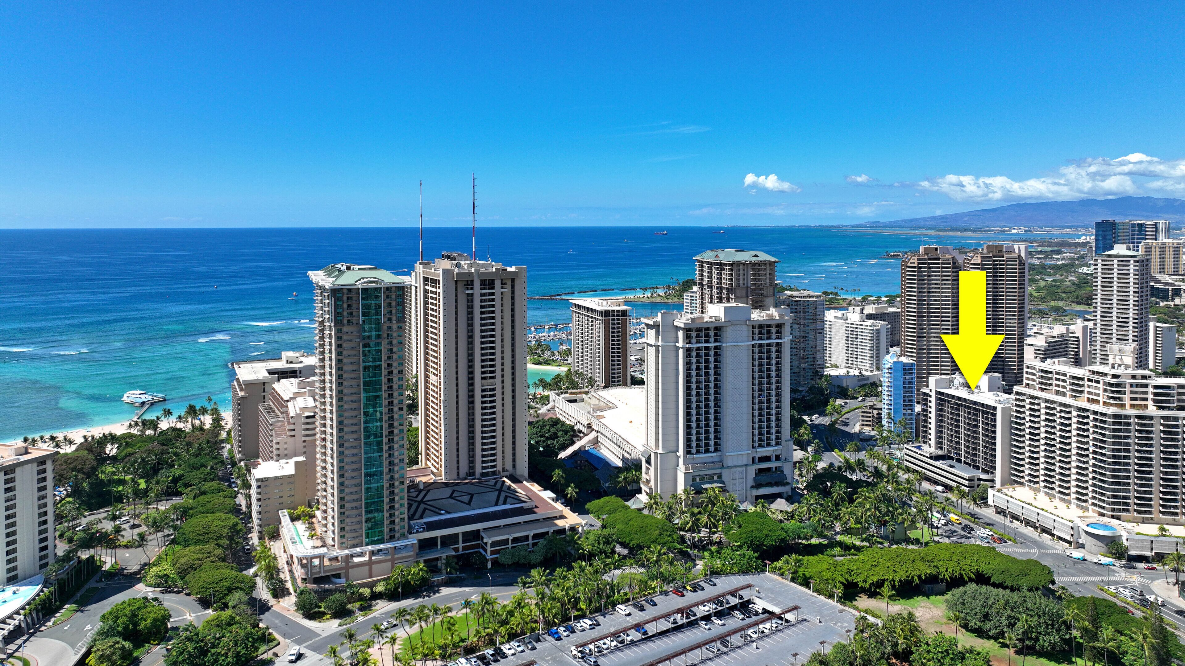 A high-rise hotel with multiple floors, a parking lot, and a view of the ocean.
