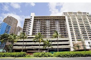 A multi-story hotel with a central atrium, surrounded by palm trees and other buildings. - Recently updated, Sleeps Four, Walk to Beach :) (Honolulu)