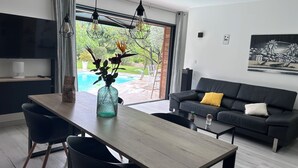 A modern living room with a dining area, a black leather sofa, and a large window overlooking a pool.
