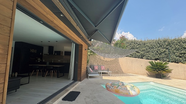 A modern house with a swimming pool, a covered patio, and a kitchen visible through an open door.