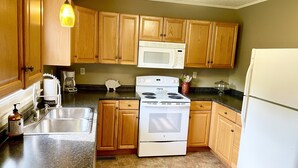A kitchen with wooden cabinets, a white stove, a microwave, a sink, and a countertop.