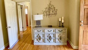 A hallway with a white dresser, a wall-mounted branch decoration, and two candle holders.