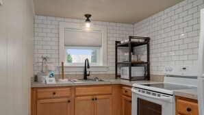 Een keuken met witte metrotegels, houten kastjes, een roestvrijstalen spoelbak en een magnetron en fornuis.