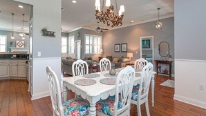 A dining area with a white table and chairs, a chandelier, and a kitchen in the background. - Treasure Beach House with private pool and dock (ST. AUGUSTINE)