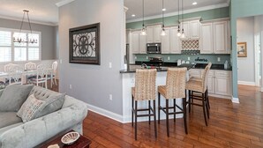 A modern kitchen with white cabinets, a central island with bar stools, and pendant lighting. - Treasure Beach House with private pool and dock (ST. AUGUSTINE)