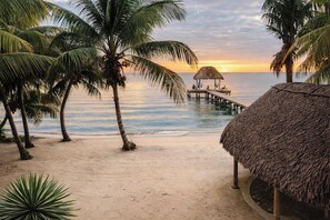 A beach with palm trees, a thatched hut, and a pier extending into the water. - Beachfront Villa with Dock & FREE Golf Cart! (Hopkins)