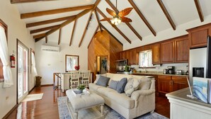 Ein geräumiges Wohnzimmer mit hohen Decken, Holzbalken, einem großen Deckenventilator und einer Küchenzeile mit Holzschränken und modernen Geräten.