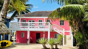 Ein zweigeschossiges Gebäude mit roter und weißer Fassade, einem Balkon mit weißen Geländern und einem Strohdach.