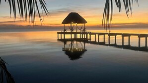 Ein ruhiger Infinity-Pool mit einer Holzterrasse und einem Gazebo mit Reetdach.