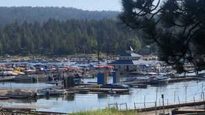 Un puerto deportivo con barcos amarrados, un pequeño edificio de techo azul y una colina boscosa al fondo.