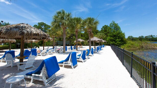 Een strandlounge met witte ligbedden en blauwe hoezen, palmbomen en een rieten constructie.