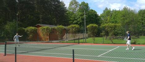 A tennis court with a net, surrounded by a fence and trees.