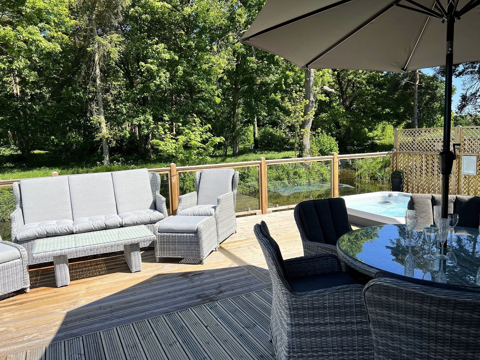 A deck with wicker furniture, a hot tub, and a glass table with wine glasses.